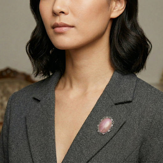 Woman wearing a gray blazer with a pink brooch against a neutral background
