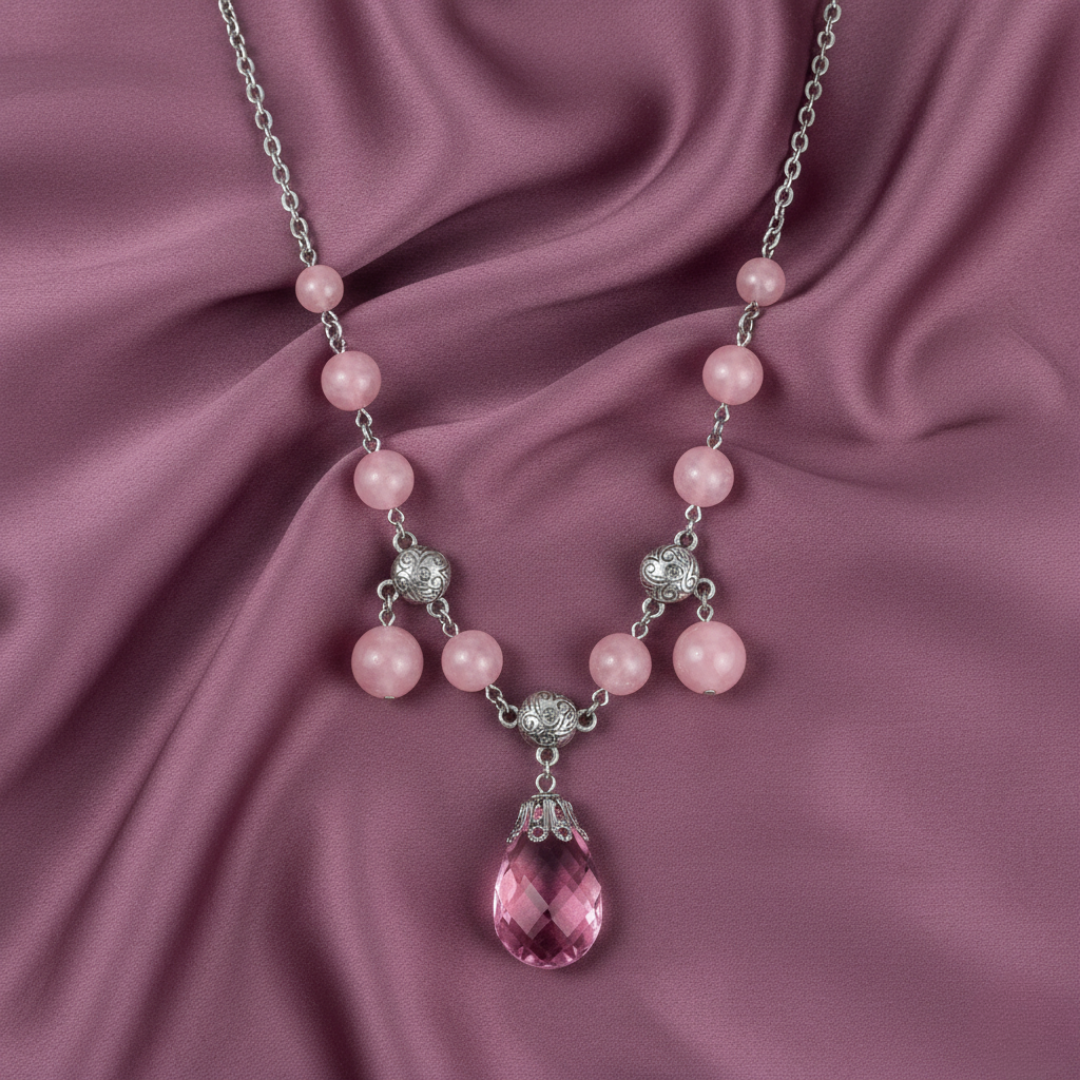 Necklace with pink beads and a teardrop-shaped pink gemstone on a pink fabric background