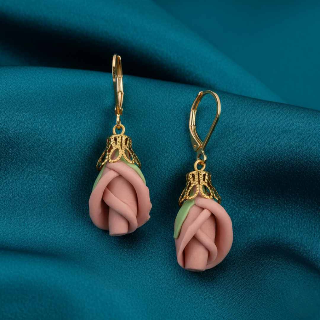 Pink rose-shaped earrings with gold accents on a teal fabric background