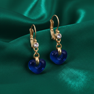 Gold earrings with blue heart charms on a green satin background