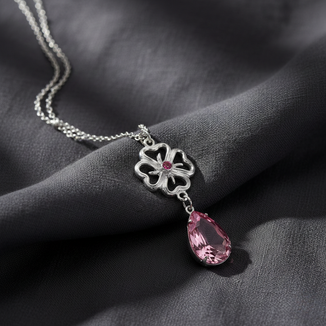 Necklace with a pink teardrop pendant and silver floral design on a dark fabric background