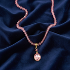 Pink beaded necklace with a pink pendant on a dark blue fabric background