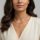 Woman wearing a pink beaded necklace with a heart pendant against a neutral background