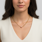 Woman wearing a gold necklace with a pink faux pearl pendant on a plain background