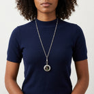 Person wearing a necklace with a locket pendant on a plain background