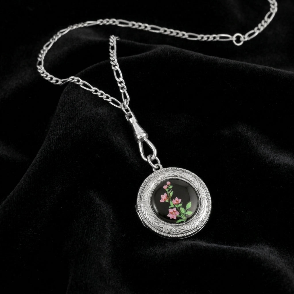 Silver necklace with a round locket pendant featuring floral design on a black fabric background