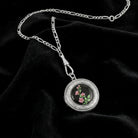 Silver necklace with a round locket pendant featuring floral design on a black fabric background
