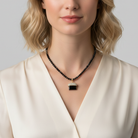 Woman wearing a black beaded necklace with a pendant against a neutral background