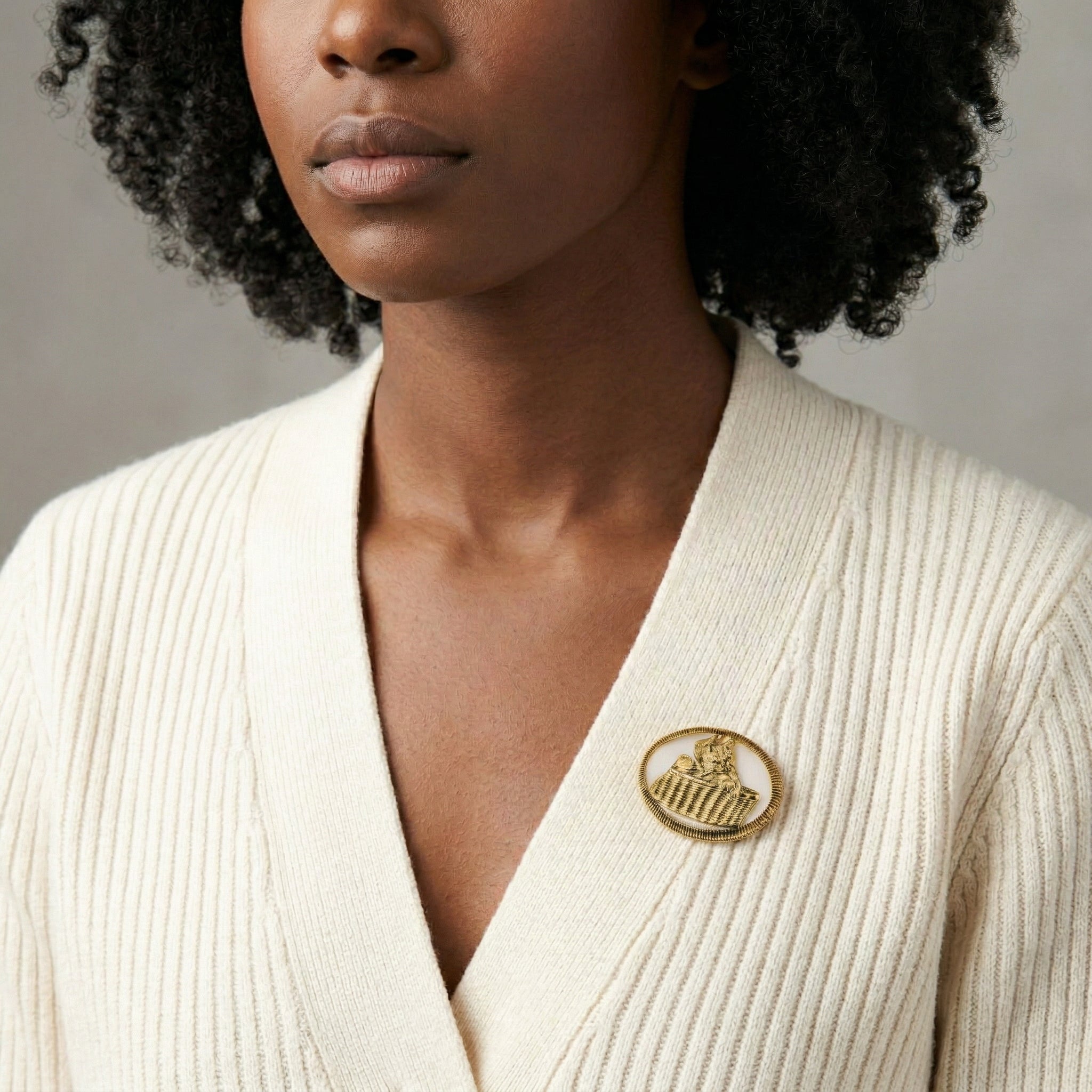Woman wearing a cream-colored cardigan with a gold brooch on a neutral background