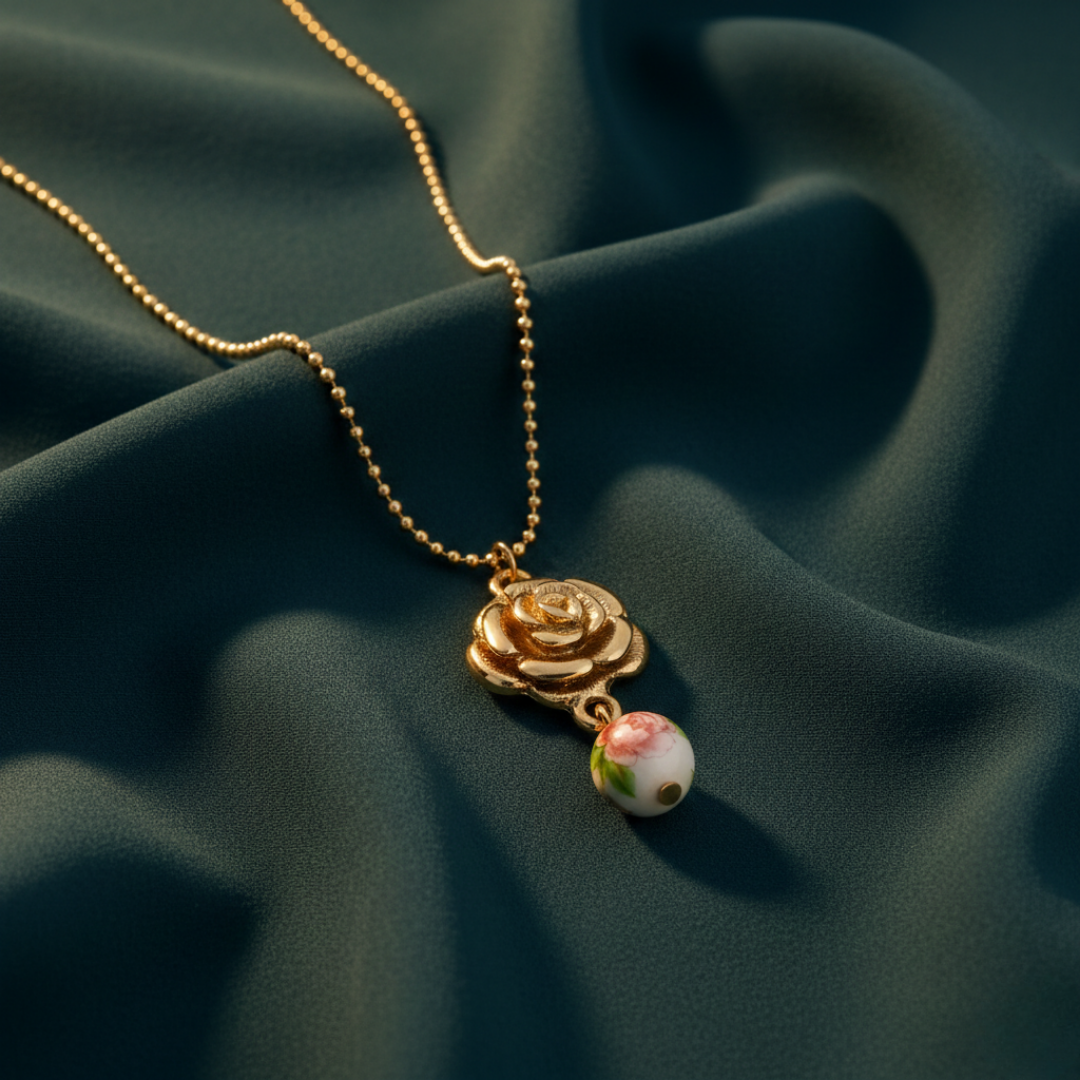 Gold necklace with a rose pendant and small bead on a dark fabric background