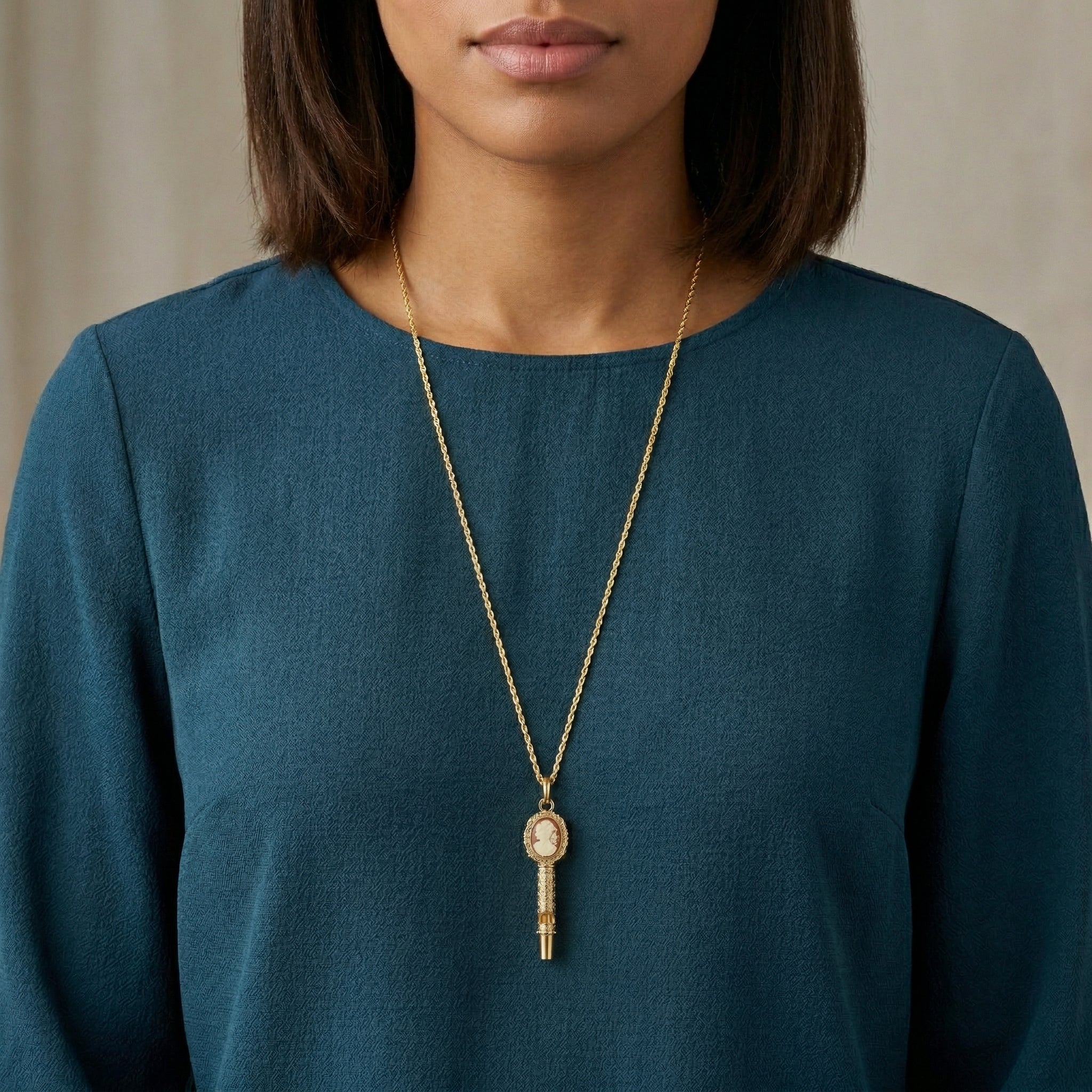 Woman wearing a gold necklace with a cameo whistle pendant against a neutral background