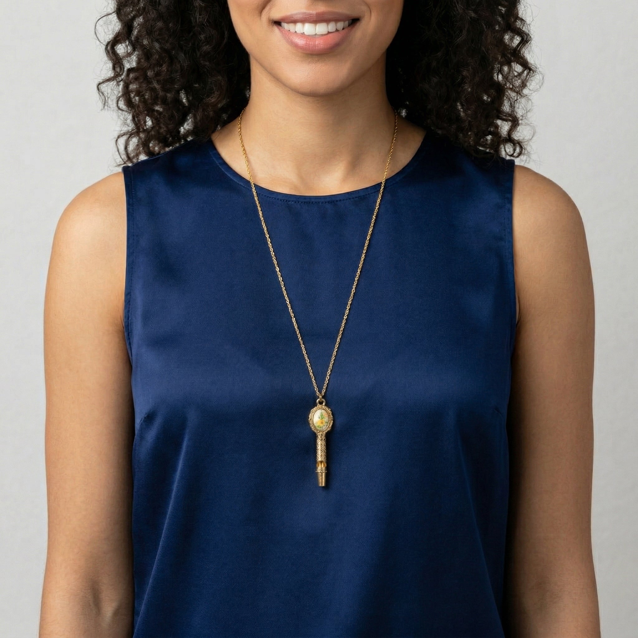 Woman wearing a gold necklace with a whistle pendant against a neutral background