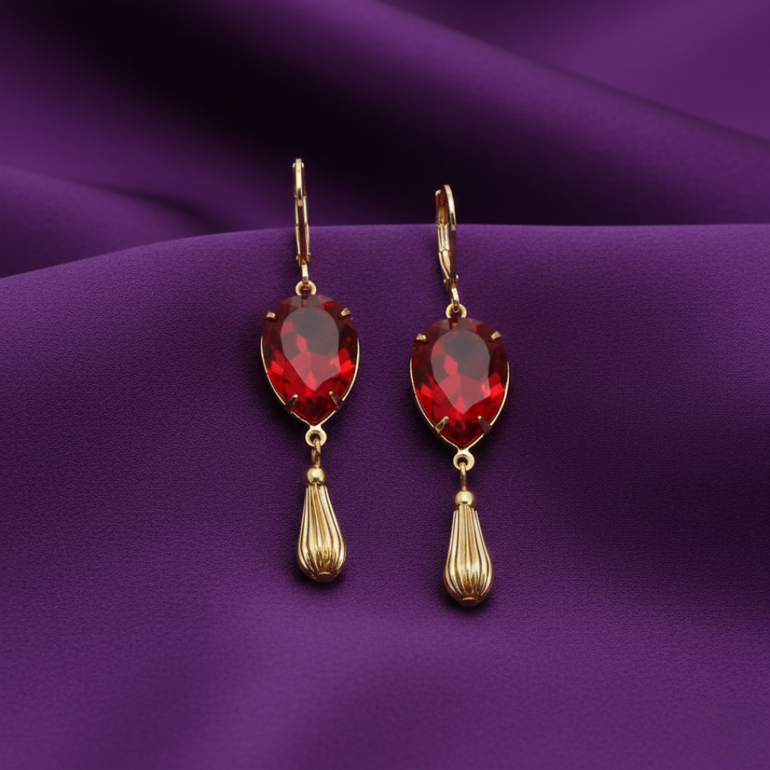 Gold earrings with red teardrop crystals on a purple fabric background