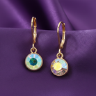 Gold earrings with colorful gemstones on a purple fabric background