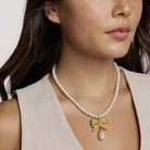 Pearl necklace with a gold bow pendant worn by a person