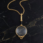Golden Era Magnification Pendant Necklace resting on black stone 