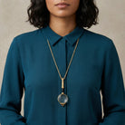 Person wearing a teal shirt with a Golden Era Magnification Pendant Necklace