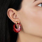Close-up of a person wearing a red hoop earring with gold accents.