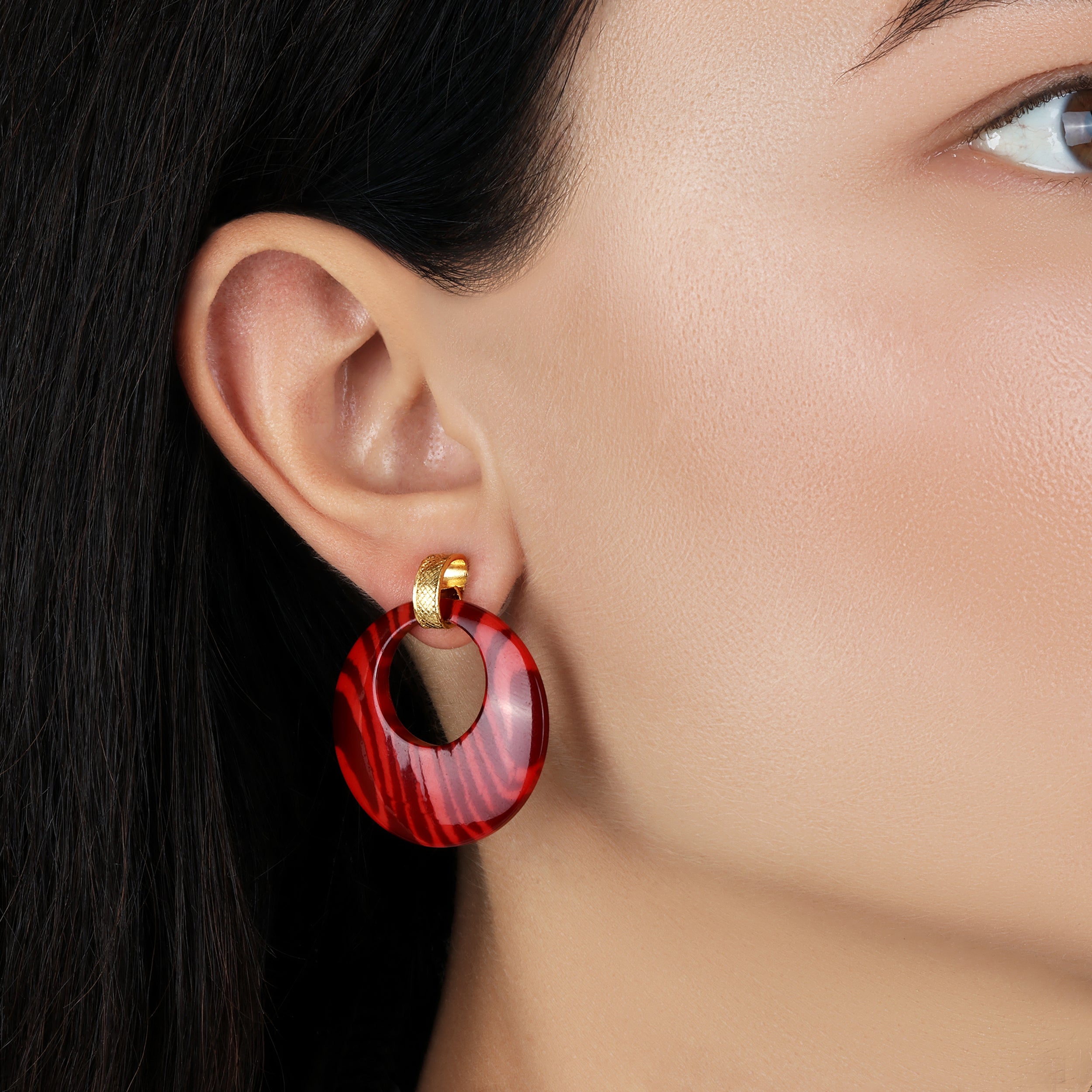 Close-up of a person wearing a red hoop earring with gold accents.