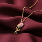 Gold necklace with a rose pink floral pendant on a red fabric. 