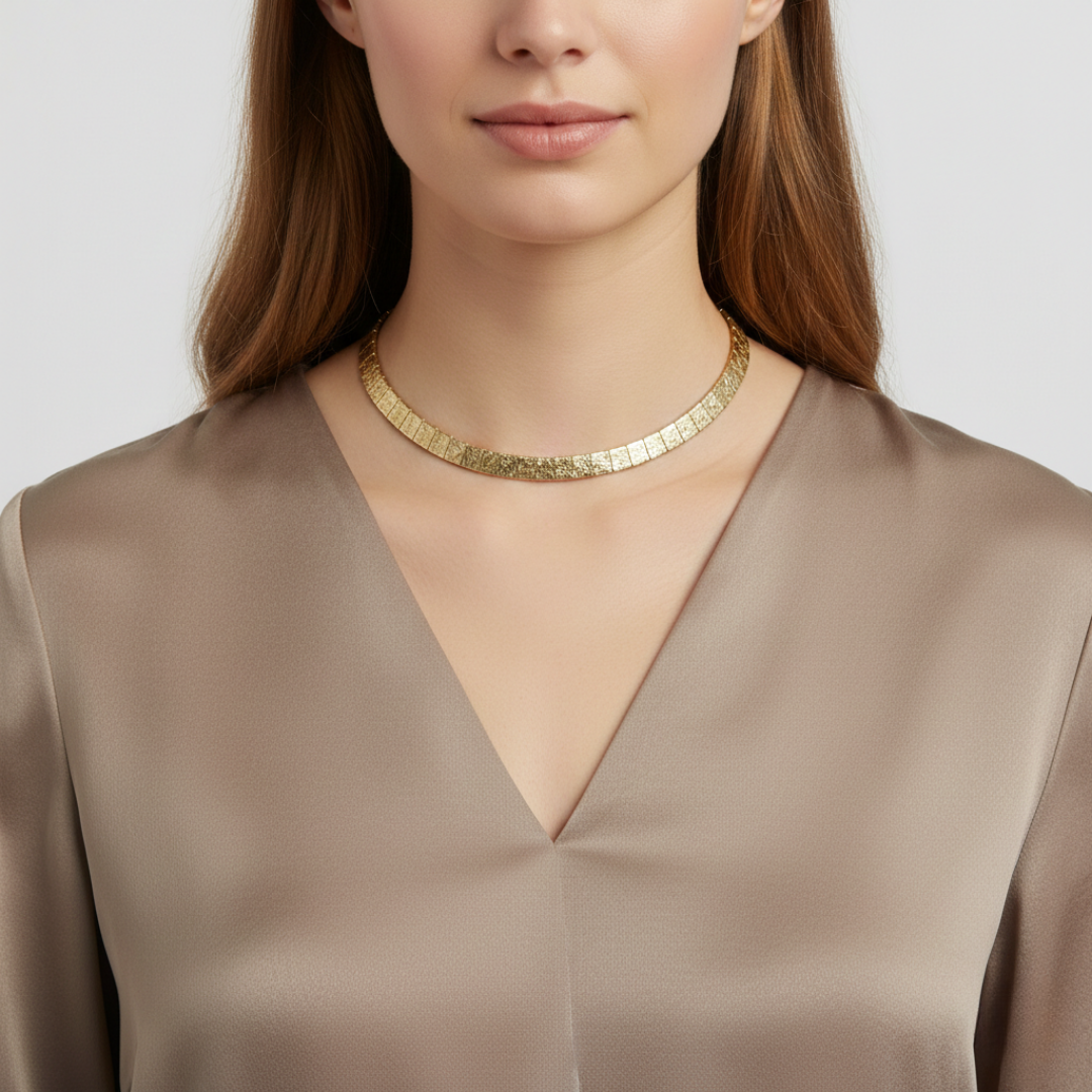 Woman wearing a gold necklace and beige top against a white background