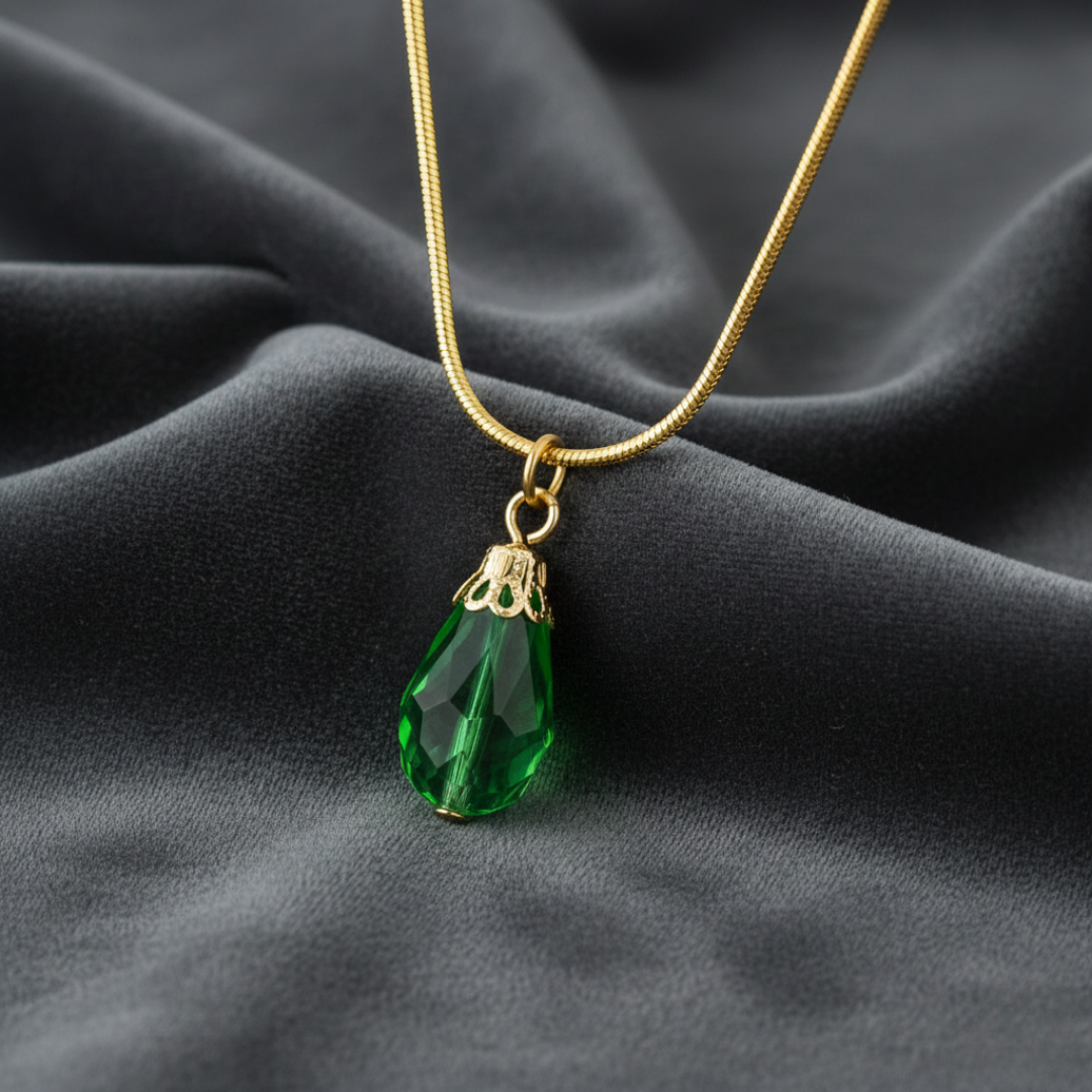 Gold necklace with a green teardrop pendant on a dark fabric background