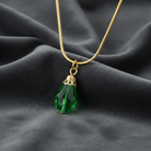 Gold necklace with a green teardrop pendant on a dark fabric background