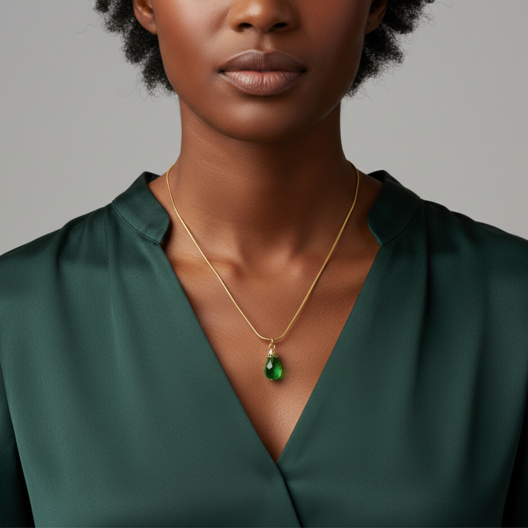 Woman wearing a gold necklace with a green pendant against a gray background