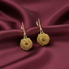 Gold rose-shaped earrings on a maroon fabric background