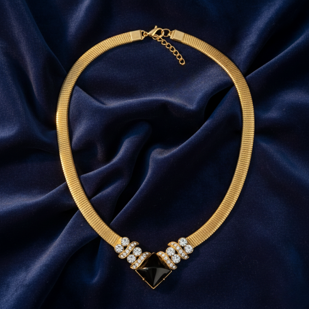 Gold necklace with a black gemstone and clear stones on a dark blue fabric background