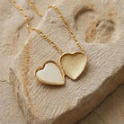 Opened gold tone Porcelain Heart Rose Motif Pendant Photo Locket Necklace on a textured stone surface