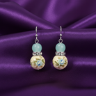 Pair of earrings with floral design on a purple fabric background
