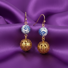 Gold earrings with blue and white spherical beads on a purple satin background