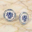 Blue Willow button earrings with light sapphire blue crystal accents resting on a marble surface. 