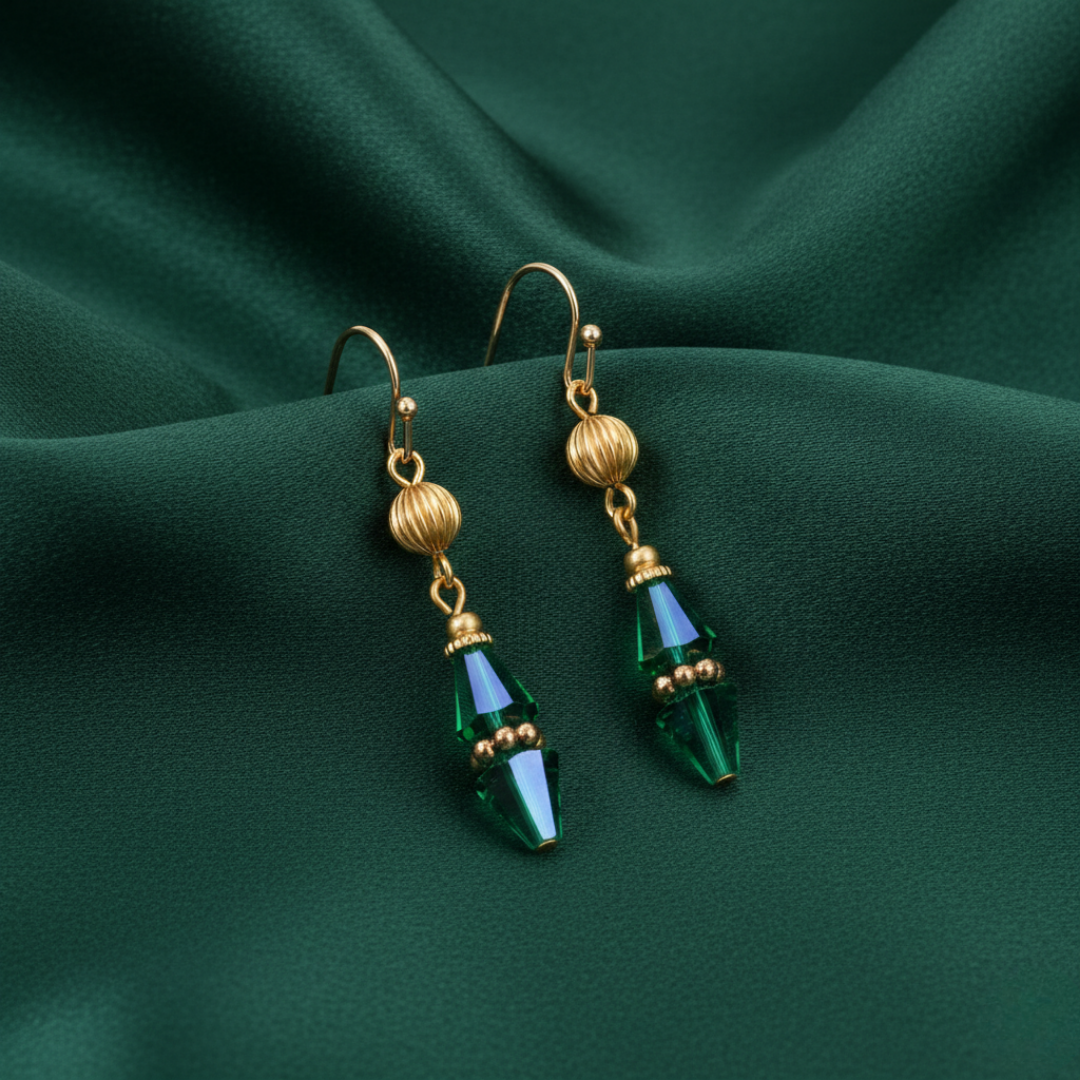 Gold earrings with green teardrop crystals on a green fabric background