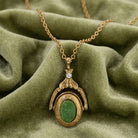 Gold necklace with a green gemstone locket pendant on a green fabric background