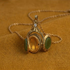 Gold pendant locket with green gemstones on a gold chain against a brown fabric background