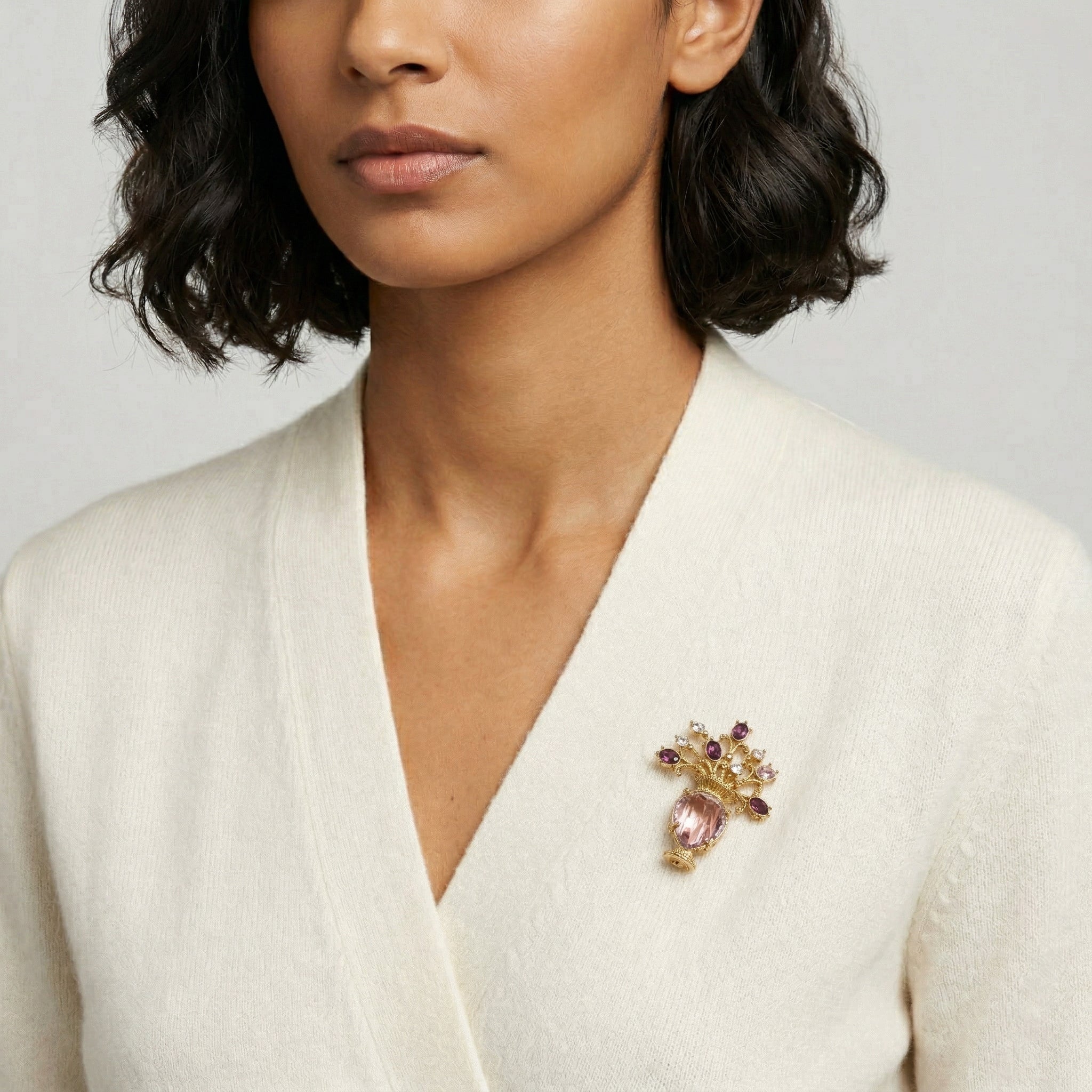 Woman wearing a white top with a decorative amethyst flower vase brooch on a plain background