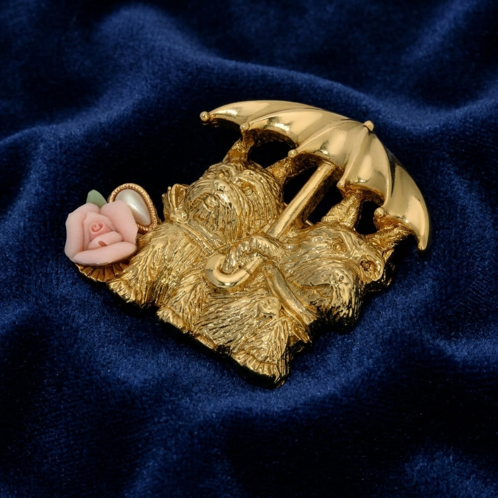 Gold brooch with two dogs holding an umbrella and a pink rose on a blue fabric background