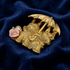 Gold brooch with two dogs holding an umbrella and a pink rose on a blue fabric background