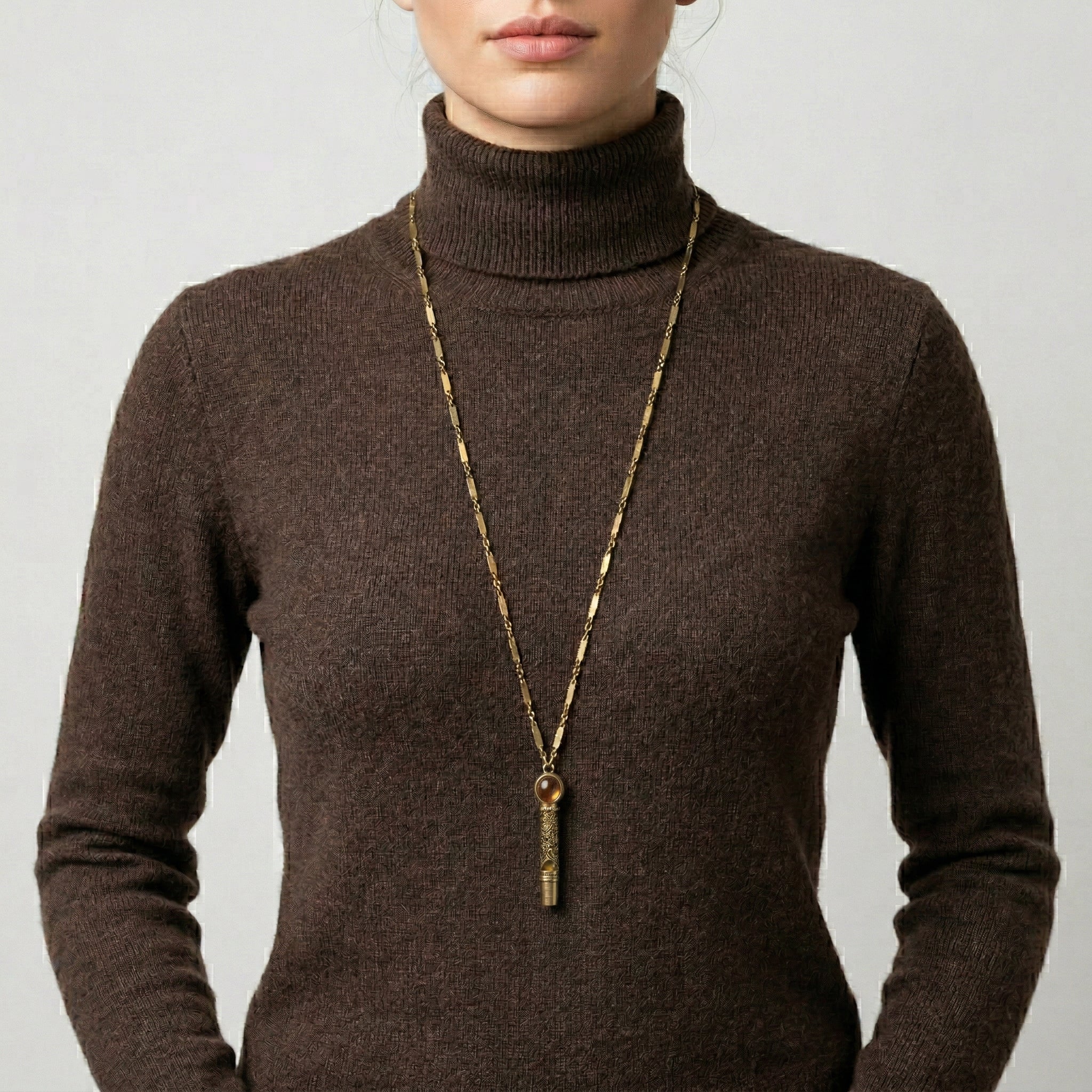 Person wearing a brown turtleneck sweater with a long gold whistle pendant necklace.