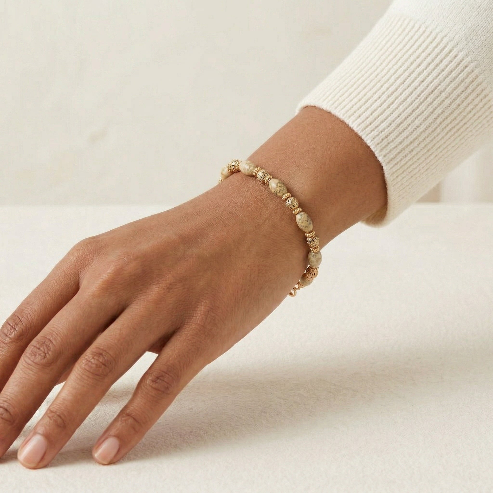Hand wearing a beaded bracelet on a neutral background