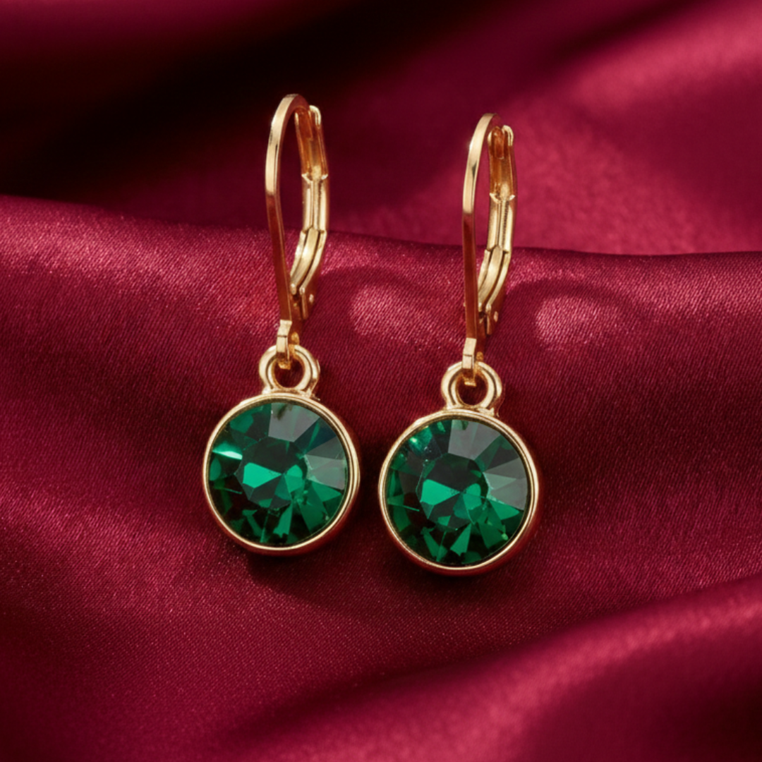 Gold earrings with green gemstones on a red satin background