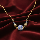 Necklace with blue and white bead and gold accents on a red fabric background