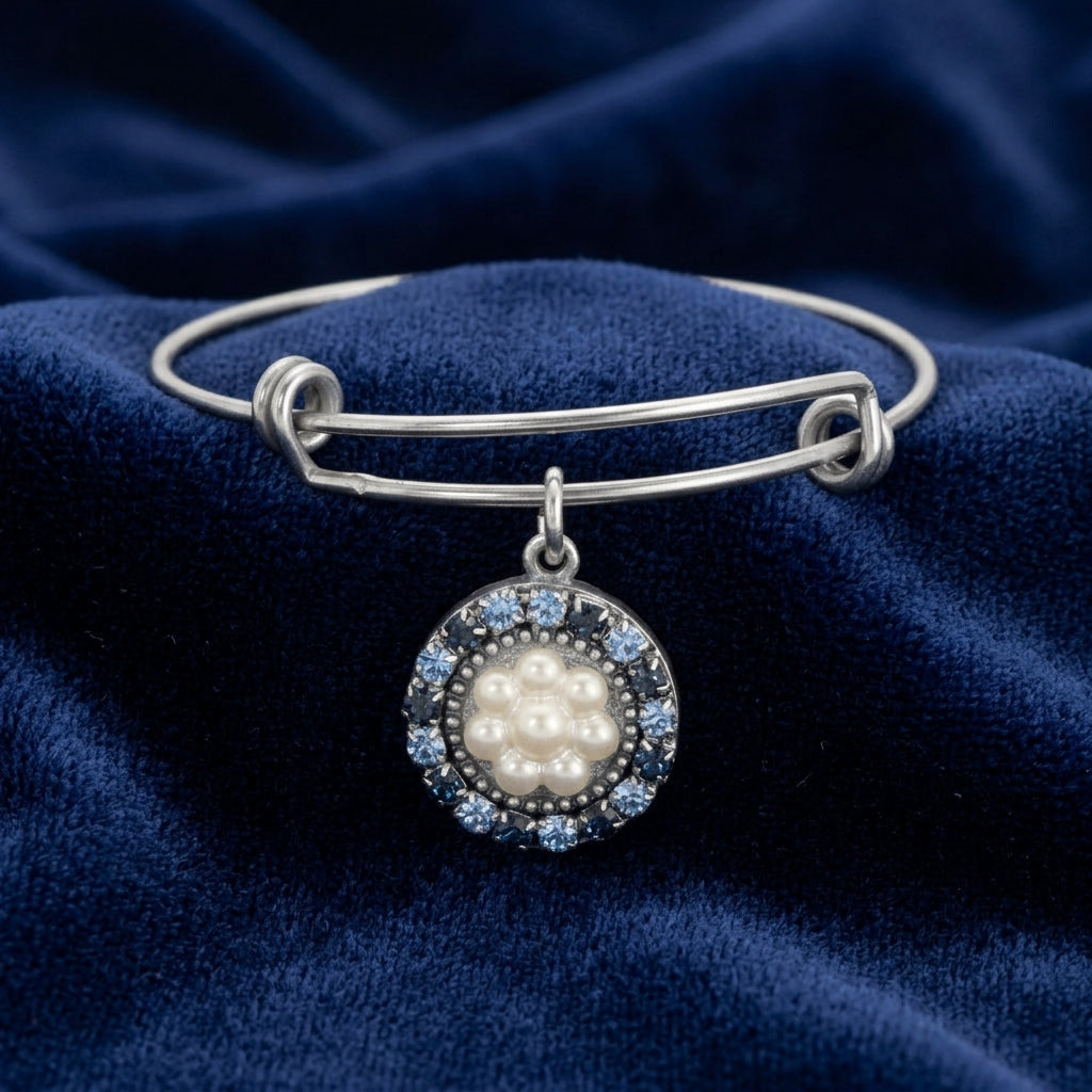 Silver bracelet with a pearl and blue gemstone charm on a blue fabric background