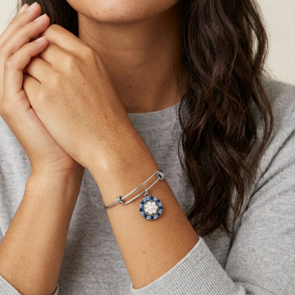Close-up of a person wearing a silver bracelet with a blue gemstone charm and faux pearls on a neutral background