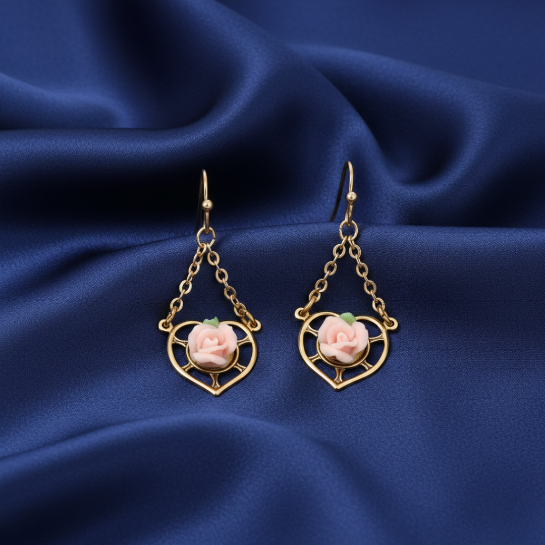 Pair of gold earrings with pink floral elements on a blue fabric background