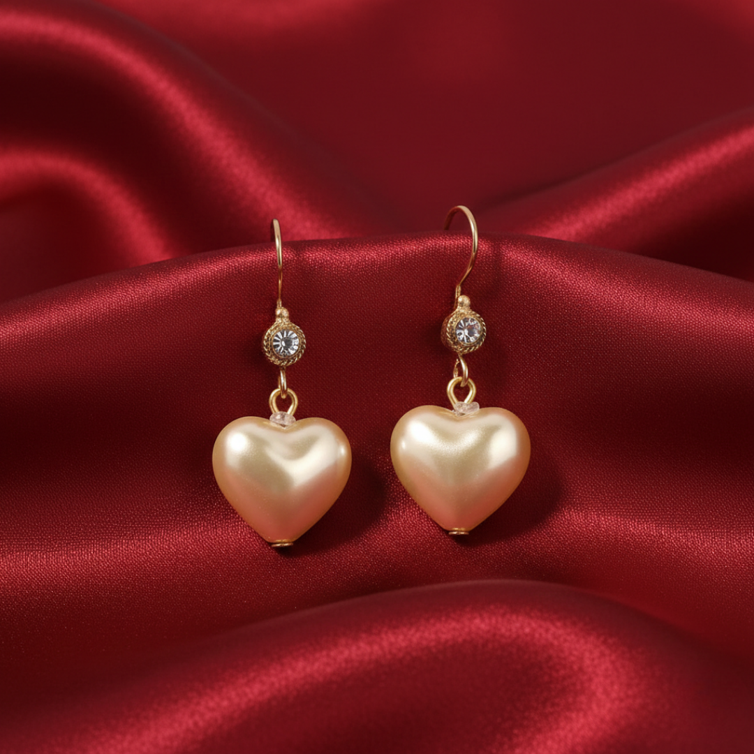 Heart-shaped faux pearl earrings with gold accents on a red satin background