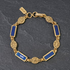 Gold tone and blue Baroque Heirloom Gold Link Bracelet on a dark gray stone surface