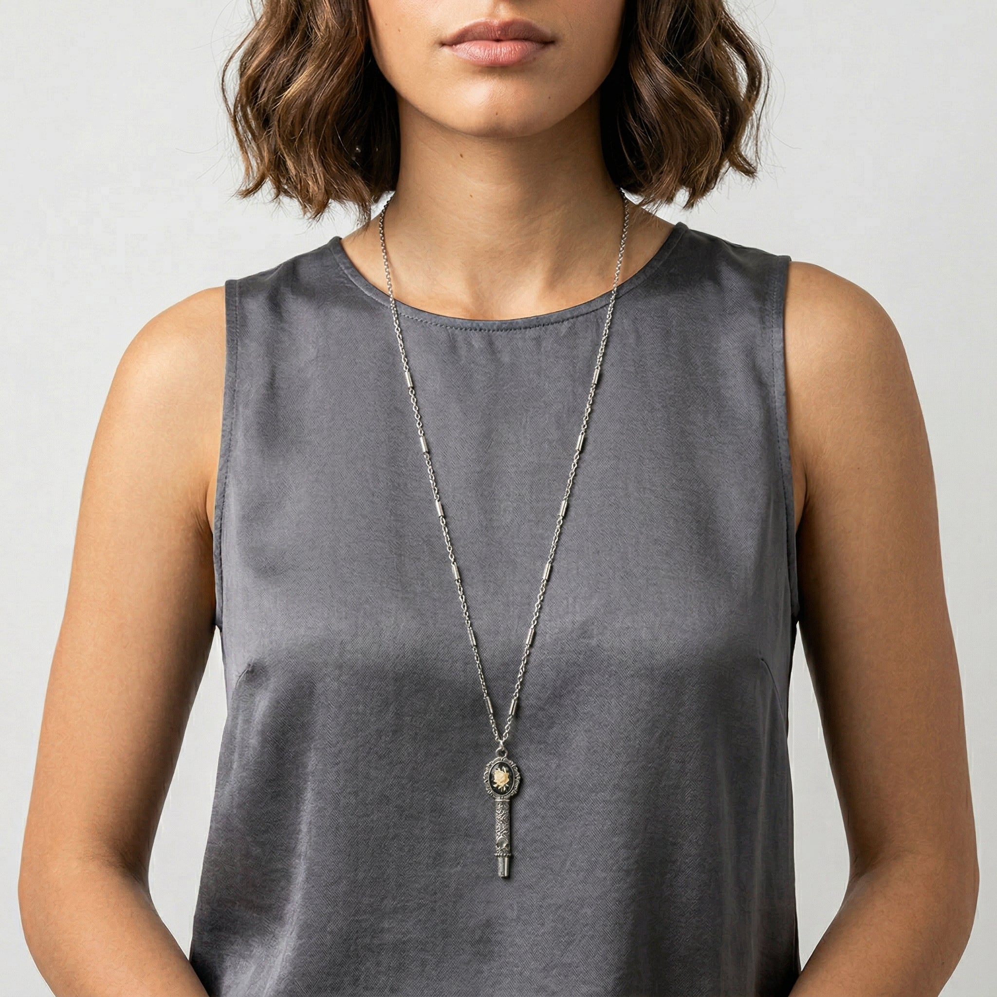 Woman wearing a long necklace with a whistle cameo pendant on a plain background
